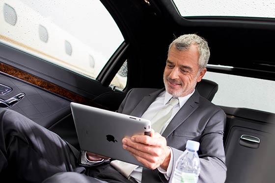 Ein Geschäftsmann sitzt in einer Business-Limousine mit einem Tablet in der Hand.